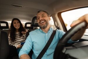 A male rideshare driver is smiling and talking to a female passenger in the back seat